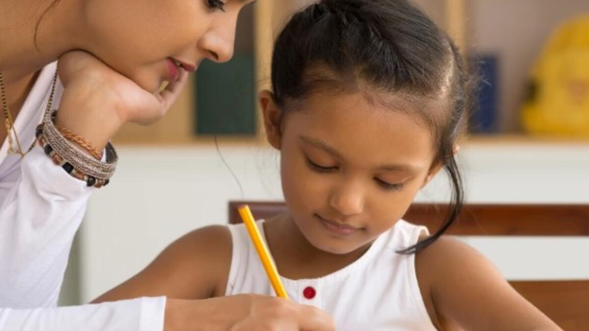 A woman assists a girl of about five with writing 