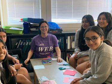 Group of students sitting at a table with teacher completing math game