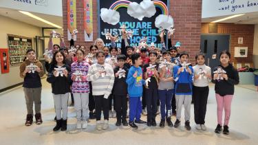 Group of elementary students standing in front foyer of school, showing of art project they completed