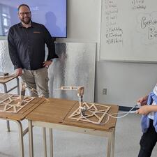 Two female students working their constructed design in Engineering class, male teacher stands and watches