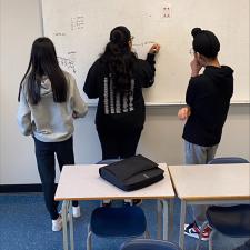 Three students working on math at the classroom whiteboard