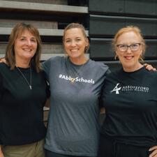 Three female volunteers pose for a photo with smiling faces, wearing shirts that represent Abbotsford School District