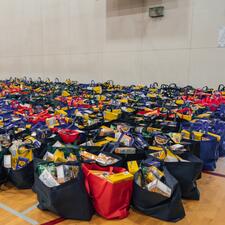 Hundreds of filled food hampers lined up in rows up against a school gymnasium wall